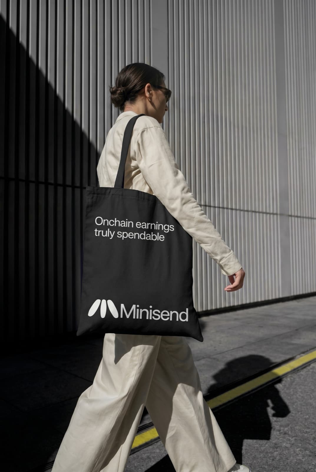 Woman walking past a ribbed wall carrying the black Minisend tote